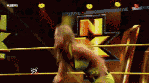 a woman is standing in a wrestling ring with the letter n on the wall behind her