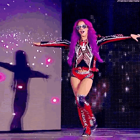 a female wrestler with purple hair and sunglasses is dancing on a stage .