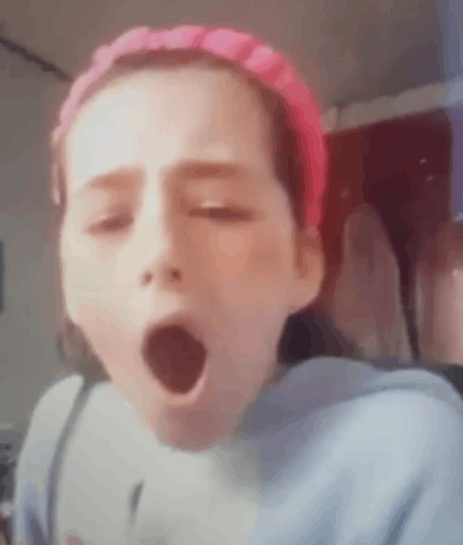 a young girl wearing a pink headband is yawning with her mouth wide open .