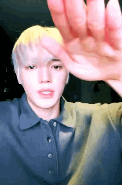 a young man with blonde hair is waving his hand in front of his face .