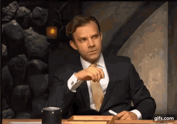 a man in a suit and tie is sitting at a table with a can of soda .