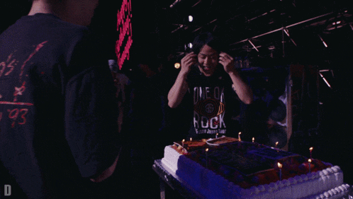 a man wearing a one ok rock shirt cuts into a cake