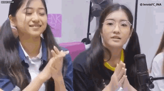two girls are clapping their hands in front of a microphone while wearing glasses .