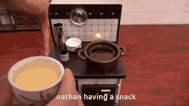 a person is holding a cup of soup in front of a stove and the words nathan having a snack