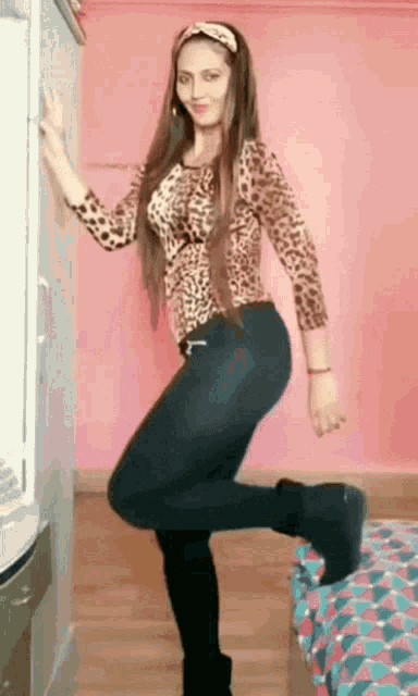 a woman in a leopard print top and black pants is standing on one leg .