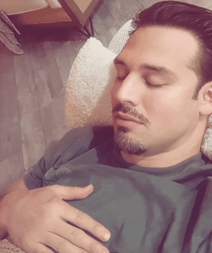 a man with a beard is sleeping with his eyes closed and his hand on his chest