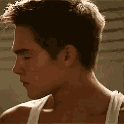 a close up of a man 's face with a white tank top on .