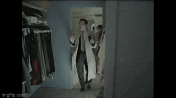a man in a white coat is standing in a closet with a woman behind him .