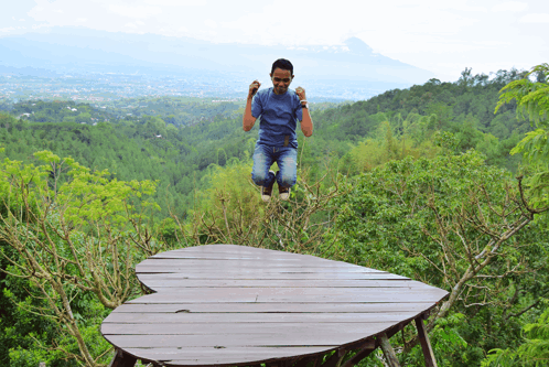 a man in a blue shirt is jumping in the air on a heart shaped wooden platform