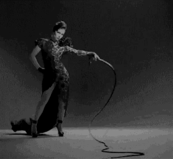 a woman in a dress is holding a whip in her hand .