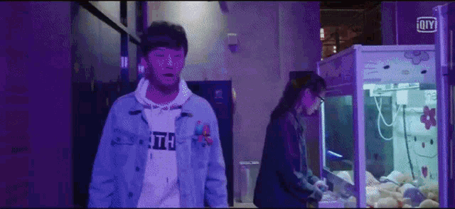a man in a denim jacket is standing next to a woman playing a game in a machine .