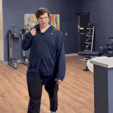 a man wearing a blue sweatshirt with a white eagle on the front walks in a gym