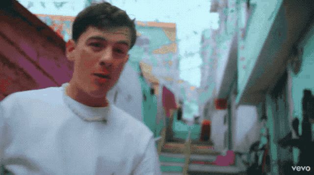 a man in a white shirt stands in a narrow alleyway with the word vevo on the bottom left