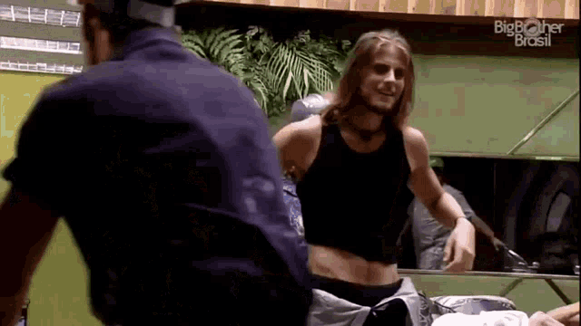 a man in a black tank top is standing next to a police officer in a room with big brother brasil written on the wall