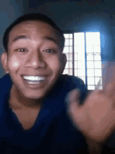 a man in a blue shirt is smiling and waving his hands