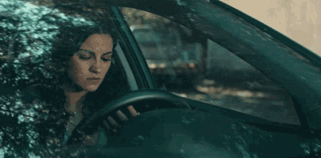 a woman is sitting in a car looking out the windshield