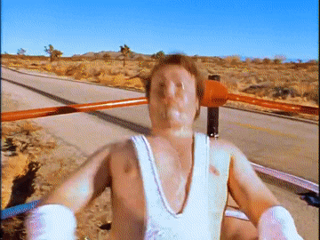 a man in a white tank top is in a boxing ring with his arms outstretched