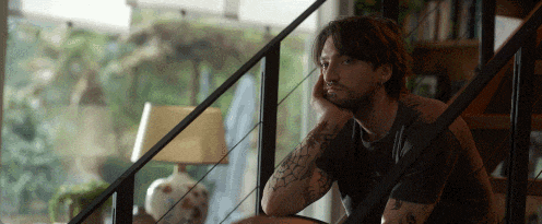 a man with a tattoo on his arm sits on a staircase