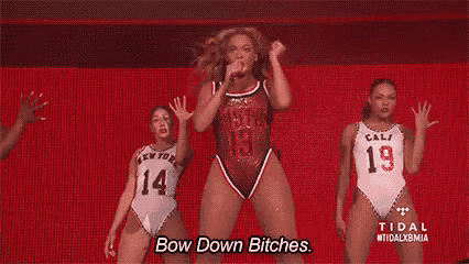 a woman in a swimsuit is dancing on a stage with two dancers and says `` bow down bitches '' .