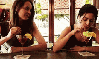 two women are sitting at a bar drinking martini 's