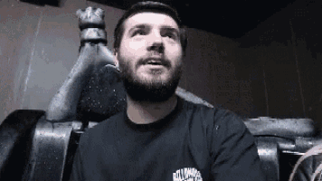 a man with a beard is sitting in a chair in front of a statue of a king .