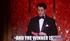 a man in a tuxedo is standing in front of a podium with the words and the winner is written below him