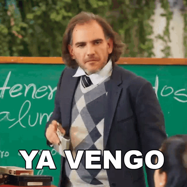 a man in a suit and tie stands in front of a green board that says ya vengo on it