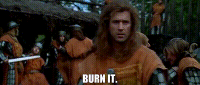a man with long hair is standing in front of a group of people holding swords and saying burn it .