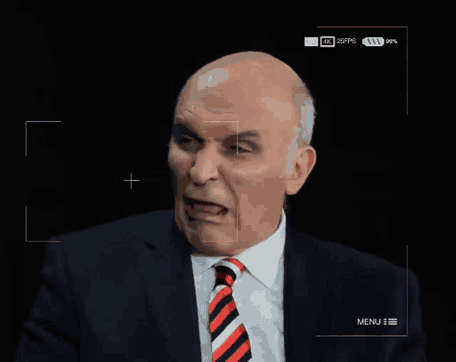 a man in a suit and tie is making a funny face with a menu visible in the corner