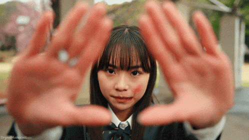 a girl with blood on her face is making a triangle with her hands .