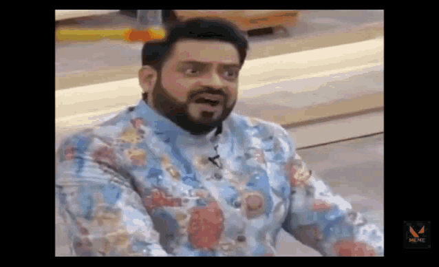 a man with a beard and a floral shirt is making a funny face while sitting down .