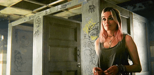 a woman with pink hair is standing next to a door in a room with graffiti on the wall .
