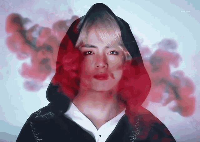 a close up of a person wearing a black hoodie with red smoke behind him