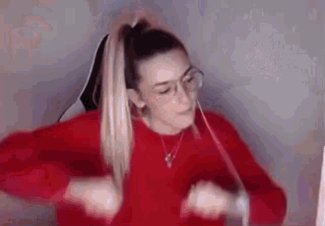 a woman wearing glasses and a red sweater is dancing in front of a computer .