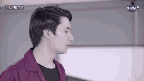 a young man in a purple shirt and black shirt is standing in front of a white wall .