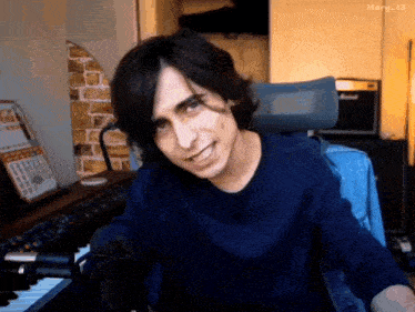 a young man in a blue shirt is sitting in front of a keyboard and smiling .