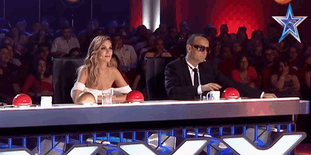 a man and a woman sit at a table in front of a crowd with a star on it
