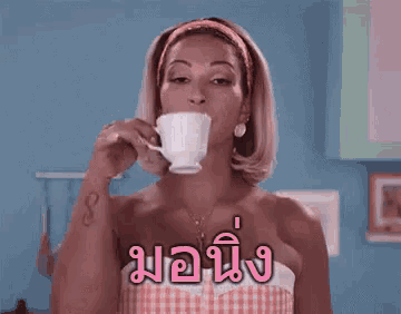 a woman is drinking a cup of coffee in a kitchen with a foreign language on her chest .