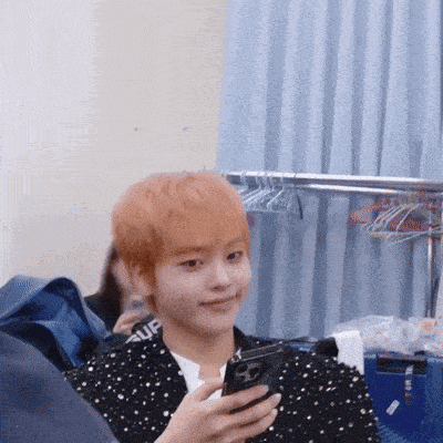 a young man with orange hair is holding a cell phone in his hand