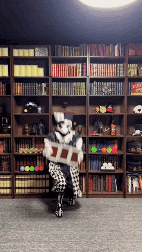 a man in a clown costume is holding a box in front of a bookshelf with a disc game on it