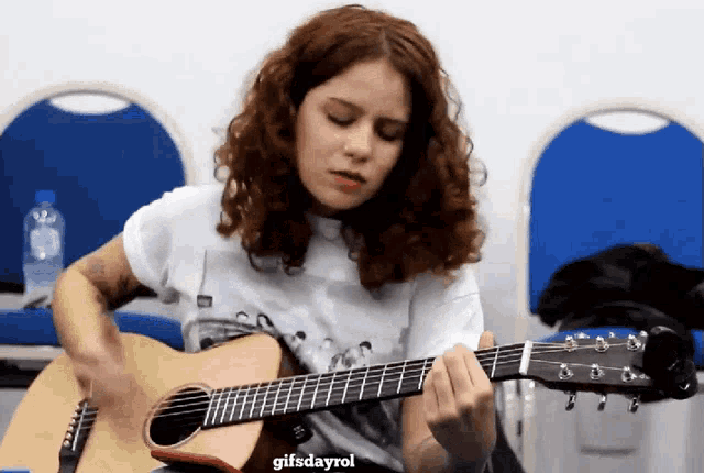 a woman playing an acoustic guitar with a gifsdayrol watermark above her