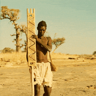 a man without a shirt is holding a wooden board with a geometric pattern on it
