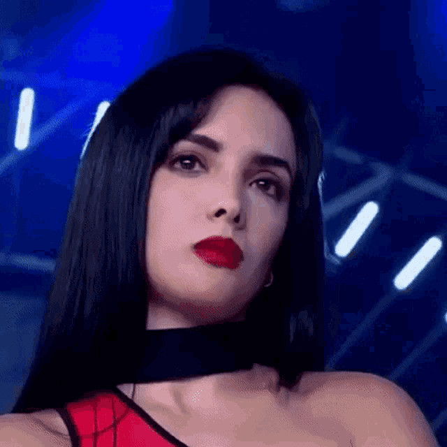 a woman with long black hair and red lipstick is wearing a red top and black choker .