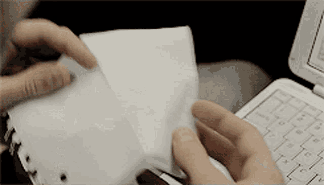 a person holding a piece of paper in front of a white laptop