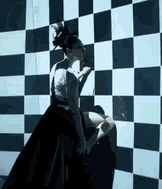 a woman in a black and white checkered dress is standing in front of a checkered wall
