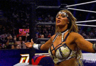 a female wrestler is standing in a wrestling ring with her arms outstretched in front of a crowd .