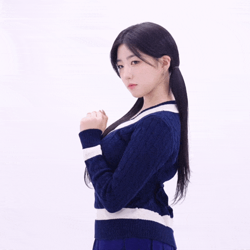 a woman in a blue and white sweater is standing with her hands folded