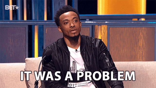a man in a leather jacket is sitting on a couch with a microphone and says it was a problem .