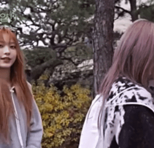 two girls are standing next to each other in a park .