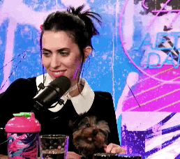 a woman is holding a small dog in her lap while speaking into a microphone